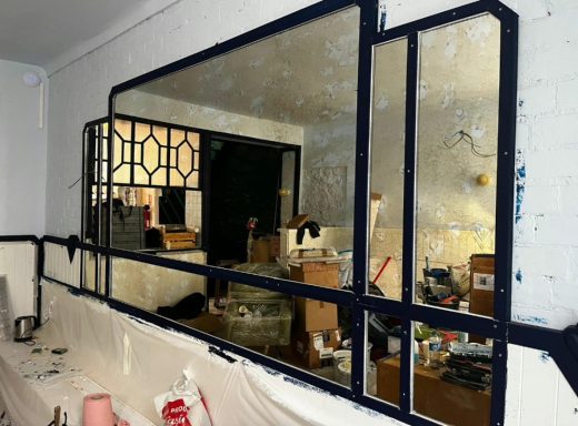 Miroir décoratif avec cadre noir, reflétant un intérieur désordonné.