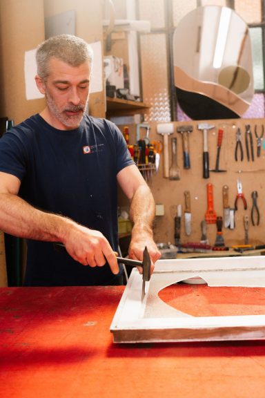 Homme utilisant un outil sur un cadre métallique dans un atelier bien éclairé.